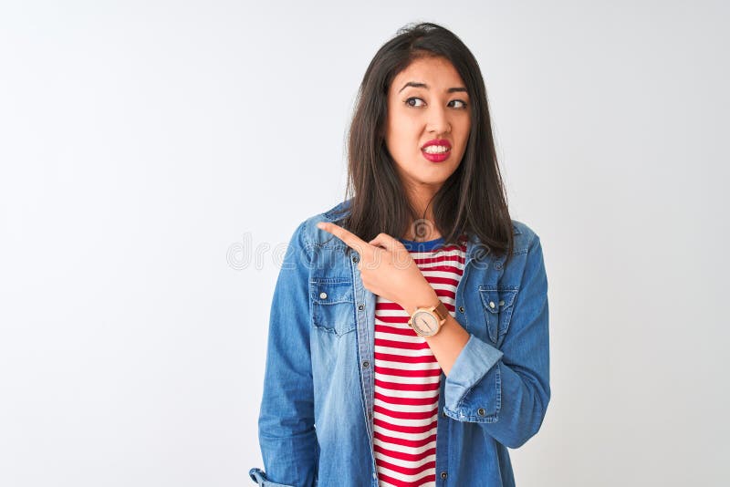 Young chinese woman wearing striped t-shirt and denim shirt over isolated white background Pointing aside worried and nervous with