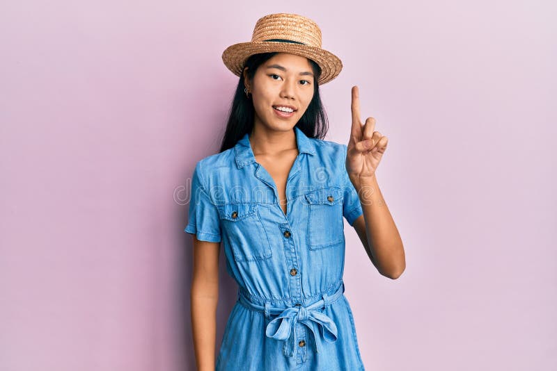 Young chinese woman wearing summer hat smiling with an idea or question pointing finger up with happy face, number one