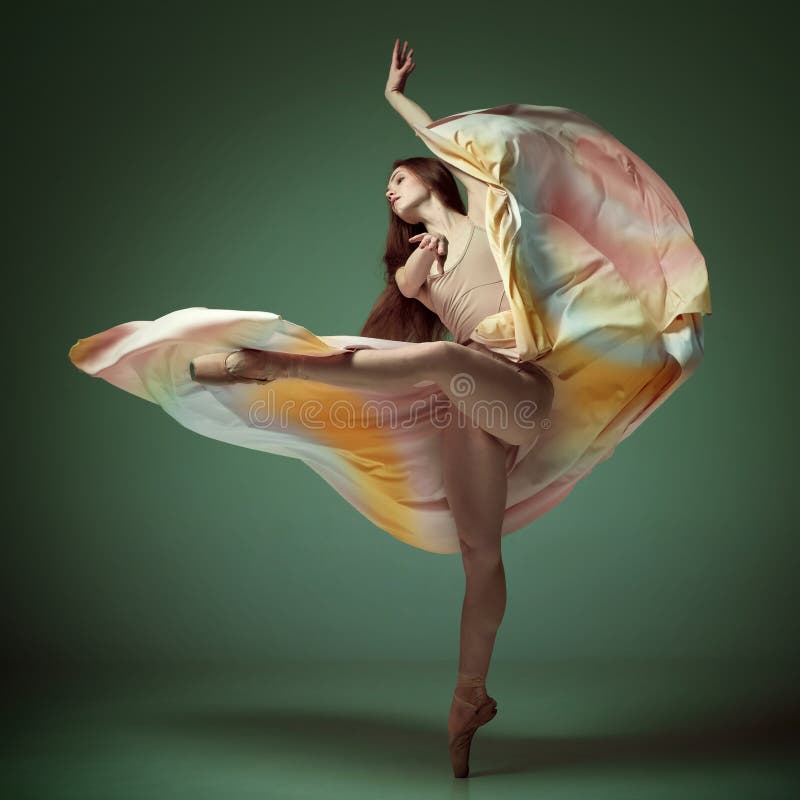 Young classical dancer wearing colorful flying dress dancing on fingertips over dark green background. Tender soul