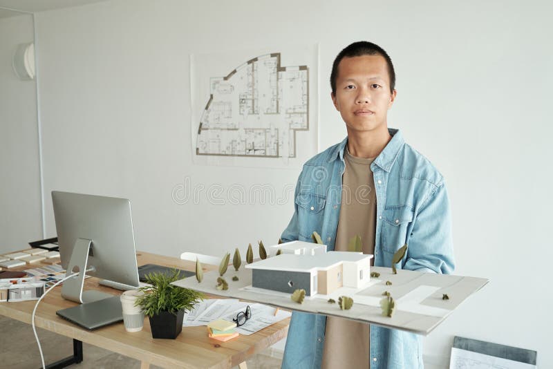 Young confident architect holding house layout against his workplace stock photography