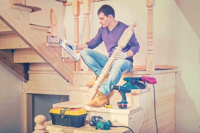 a young construction contractor sitting on steps of wooden ladder and looking on blueprint in clipboard instagram stile