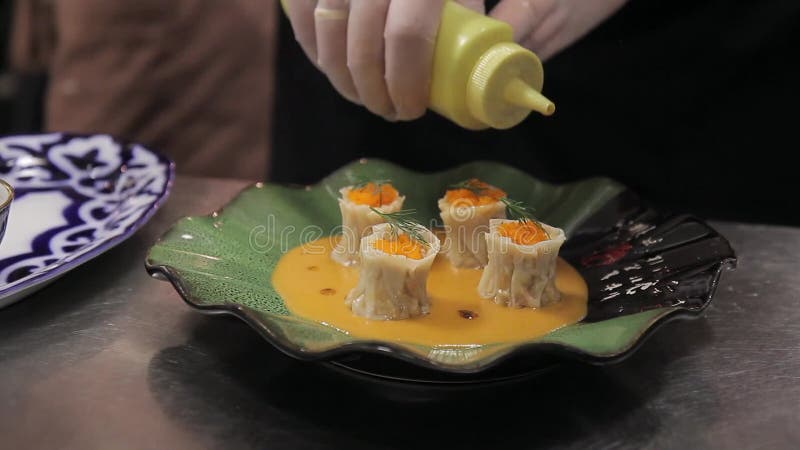 Young cook decorates cooked dish with soy sauce in kitchen of restaurant.