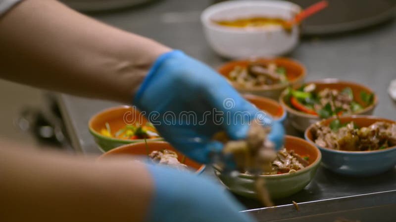 Young cook is putting meat dish in plates at table in restaurant kitchen irrl.