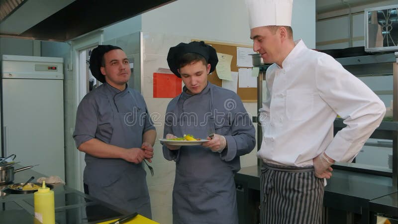 Young cook trainees tasting seafood dish made by chef