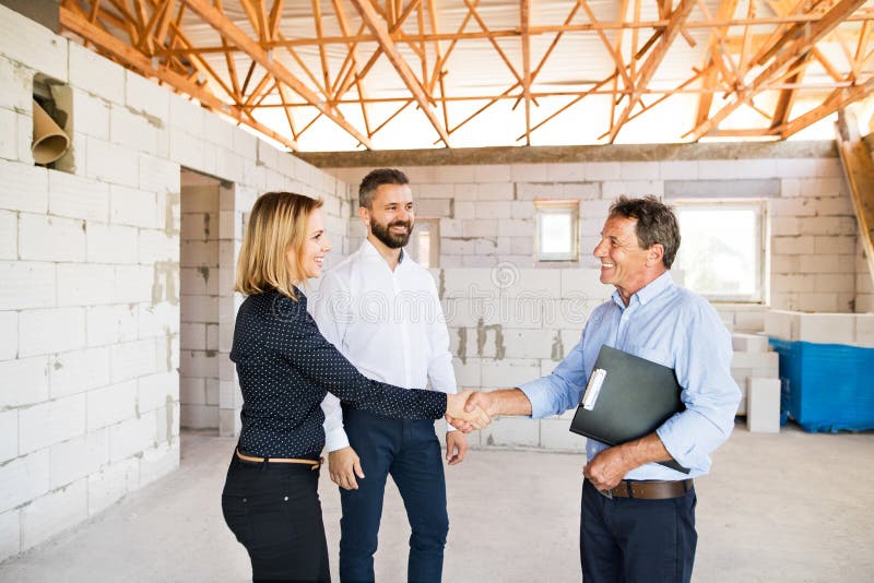 Young couple with architect or civil engineer looking at plans of their new house, discussing issues at the construction site. Young couple with architect or civil engineer looking at plans of their new house, discussing issues at the construction site.