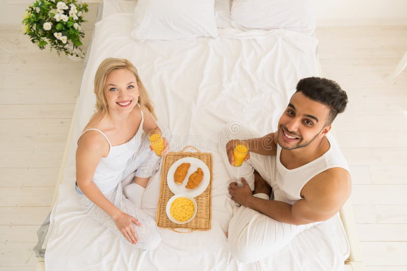 Young Couple Breakfast Sitting In Bed, Happy Smile Hispanic Man And Woman Morning Top Angle View. Male, husband.