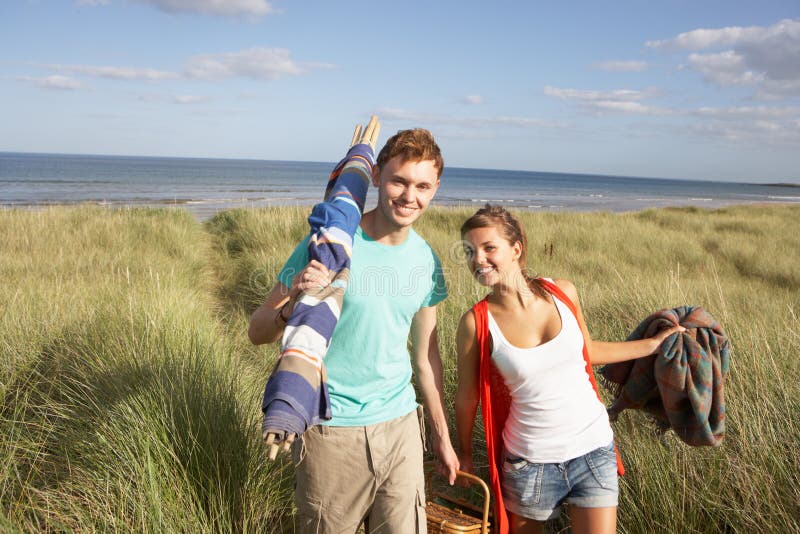 Young Couple Carrying Picnic Basket And Windbreak