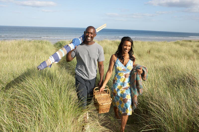 Young Couple Carrying Picnic Basket And Windbreak