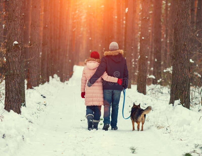 Giovane coppia felice con il cane a piedi nel bosco d'inverno torna alla fotocamera.