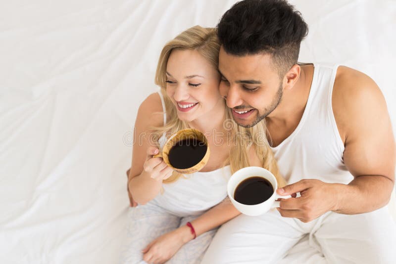 Young Couple Drink Coffee Sitting In Bed, Happy Smile Hispanic Man And Woman Top Angle View. Girlfriend, morning.