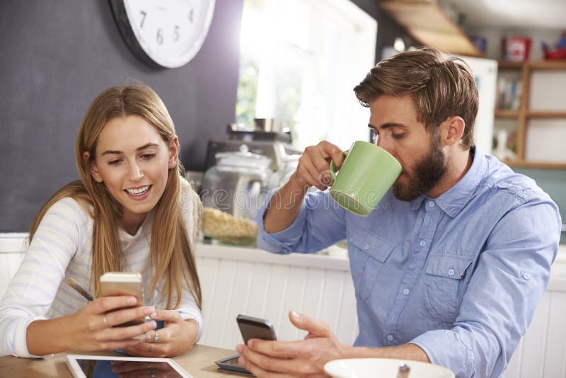 Young Couple Eating Breakfast Whilst Using Mobile Phones stock photos Young Couple Eating Breakfast Whilst Using Mobile Phones stock photos