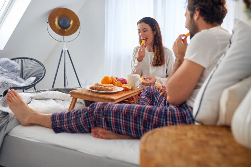 A young couple eating delicious oranges during a breakfast in the bed at their bedroom. Love, relationship, together