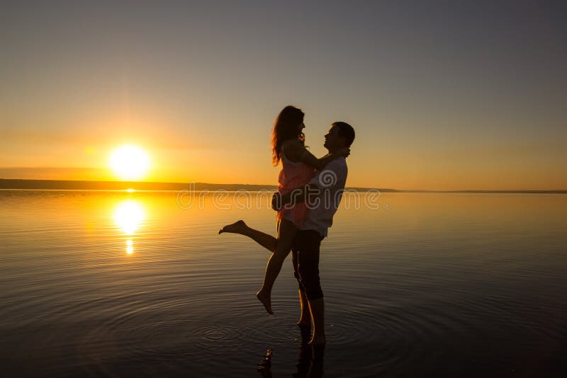 Young couple is embracing in the water on summer beach. Sunset over the sea.Two silhouettes against the sun. Just married couple