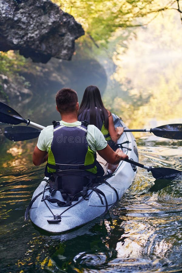 A young couple enjoying an idyllic kayak ride in the middle of a beautiful river surrounded by forest greenery royalty free stock photography