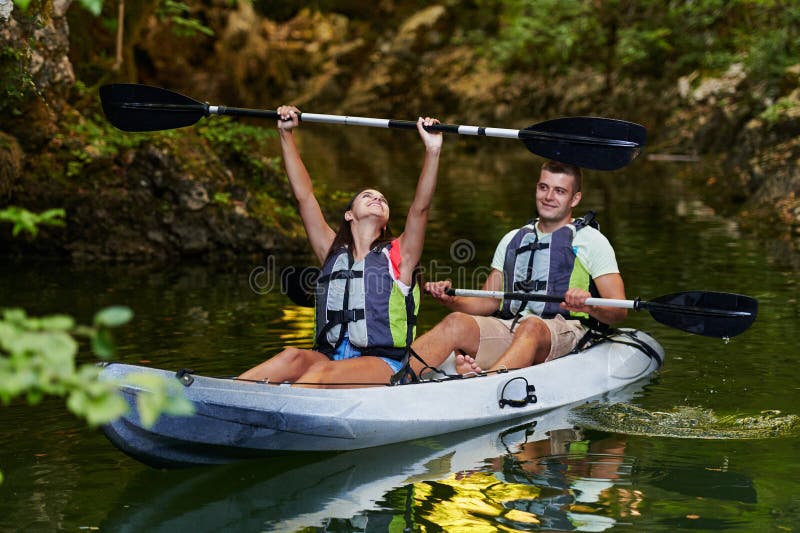 A young couple enjoying an idyllic kayak ride in the middle of a beautiful river surrounded by forest greenery royalty free stock photo
