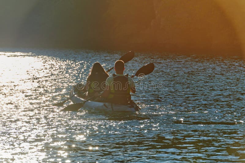 A young couple enjoying an idyllic kayak ride in the middle of a beautiful river surrounded by forest greenery in sunset royalty free stock photo