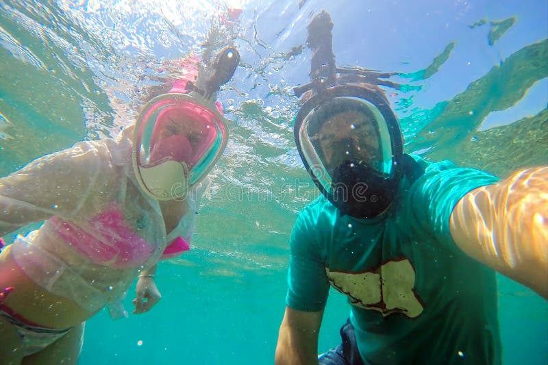 Young couple in full face masks for snorkeling making selfie under water