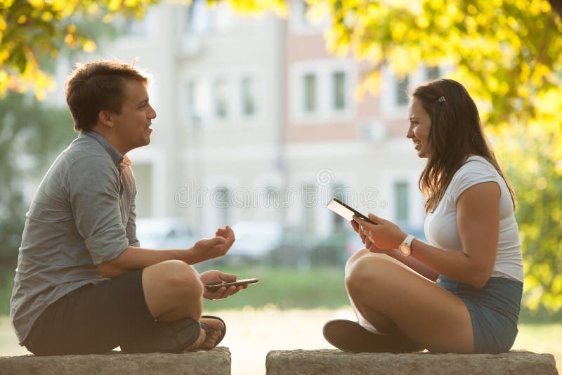 Young couple having fun on a bench in park while socializing over web