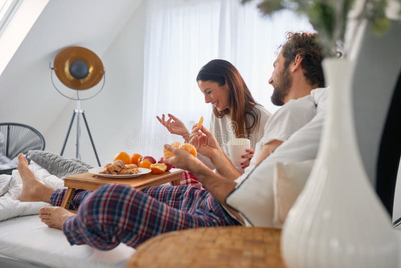 A young couple having fun while eating delicious food for a breakfast in the bed at their bedroom. Love, relationship, together