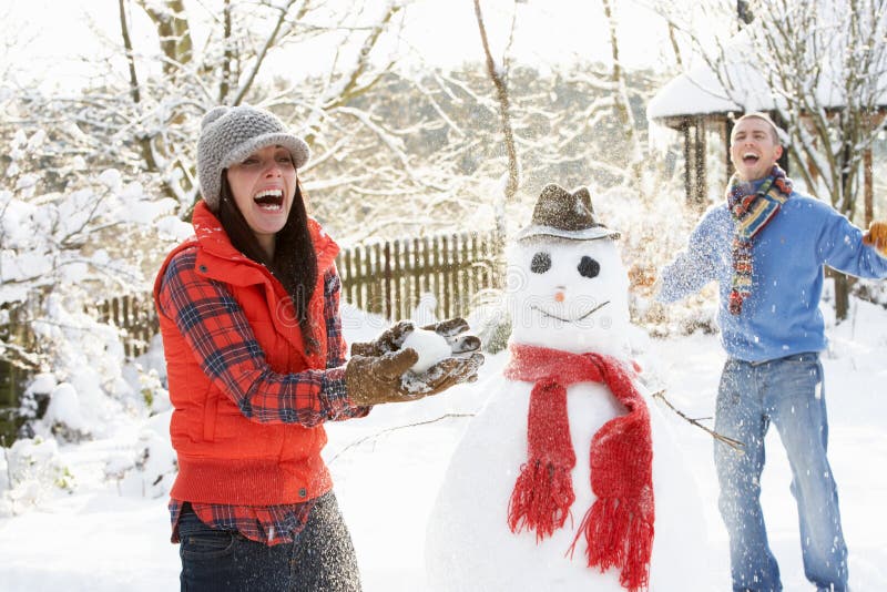 Young Couple Having Snowball Fight In Garden