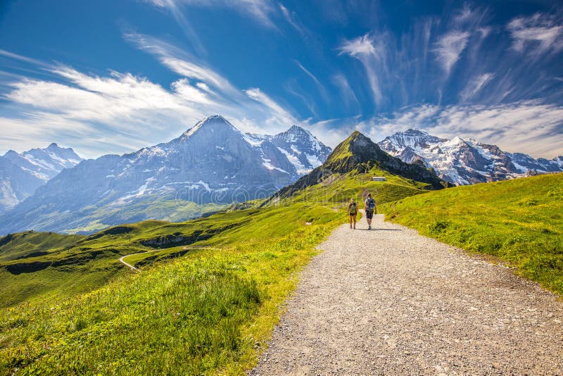 Young couple hiking in panorama trail leading to Kleine Scheidegg from Mannlichen with Eiger, Monch and Jungfrau mountain