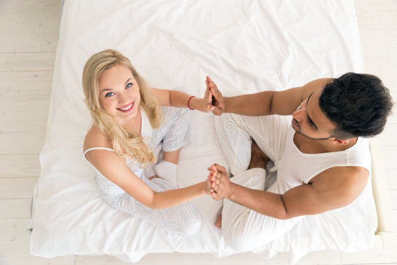 Young Couple Hold Hands Sitting In Bed, Happy Smile Hispanic Man And Woman Top Angle View.