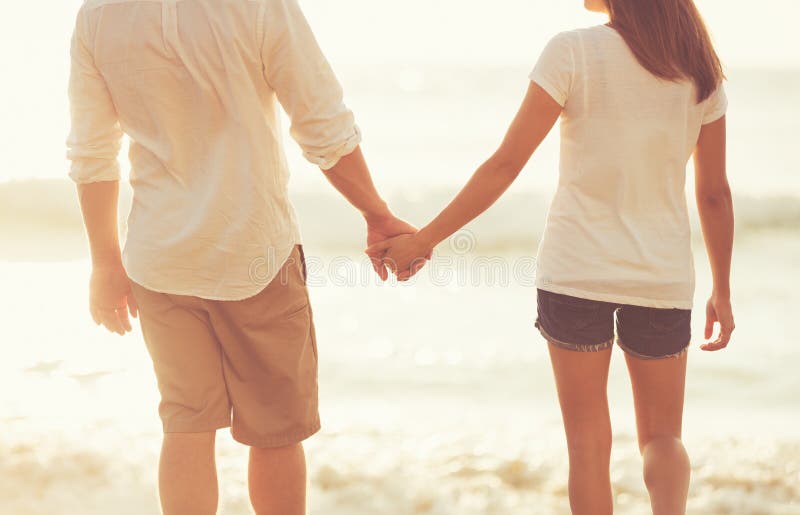 Young Couple Holding Hands on the Beach at Sunset royalty free stock photo