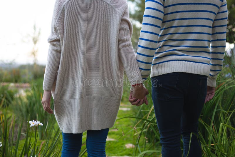 Rear view mid section of a Caucasian couple holding hands and walking in the garden. Home and lifestyle weekend activities. Rear view mid section of a Caucasian couple holding hands and walking in the garden. Home and lifestyle weekend activities.