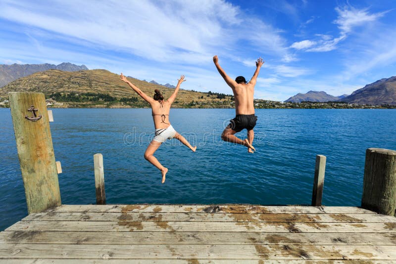 Young couple jumping on the edge of a dock in to the lake