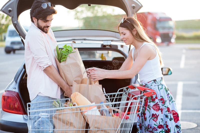 Young couple loading grocery bags into a car trunk