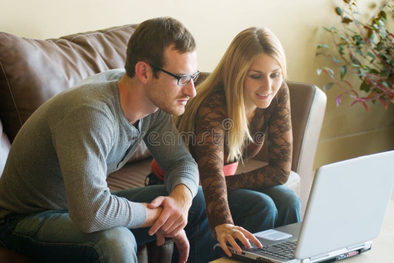 Giovane e attraente l'uomo e la donna seduta su un divano guardando un computer portatile insieme.