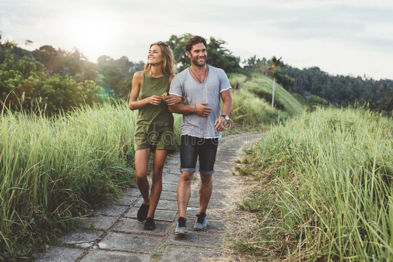 Outdoor shot of young couple in love walking on pathway through grass field. Man and women walking along tall grass field.