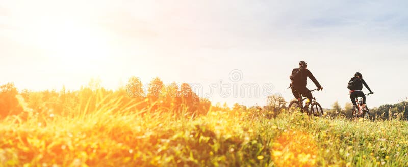 Young couple man and woman bicyclists with backpacks riding under sunset light at the early warm autumn time.  Active sport people