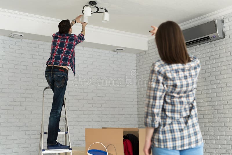 Young Couple Moving in New House, Changing a Light Bulb Stock Image