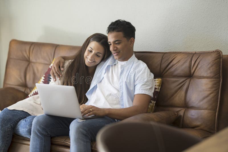 Young couple moving to a new home relaxing sitting on the sofa using computer laptop, smiling happy for moving to new apartment stock image