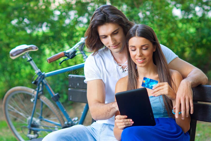 Young couple on the park bench with credit card and tablet