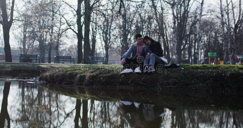 Young Couple partage un moment d'appel d'offres près de l'étang dans un parc serein banque de vidéos