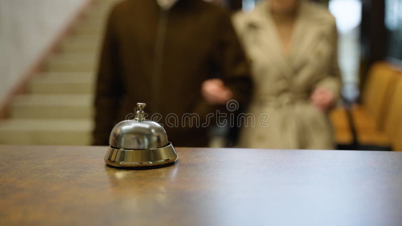 Young couple ringing hotel service bell at reception desk, close up