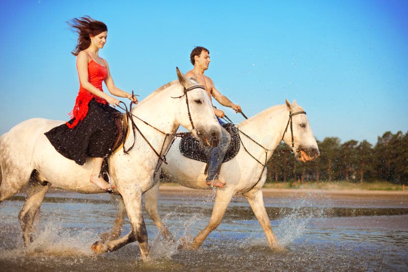 Young couple in the sea on horseback