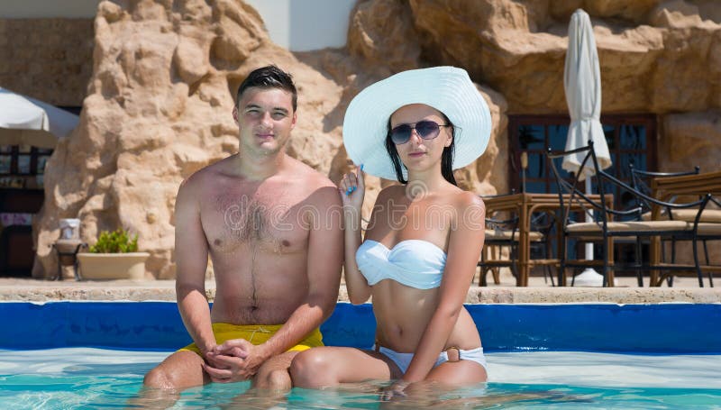 Young couple sitting on the edge of swimming pool