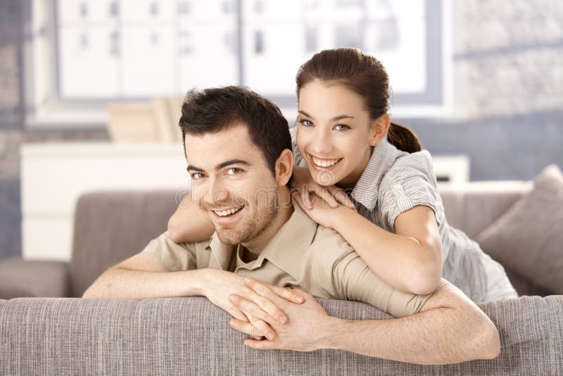 Young couple smiling happily on sofa, hugging each other at home. Happy embracing couple stock images, royalty-free photos and pictures
