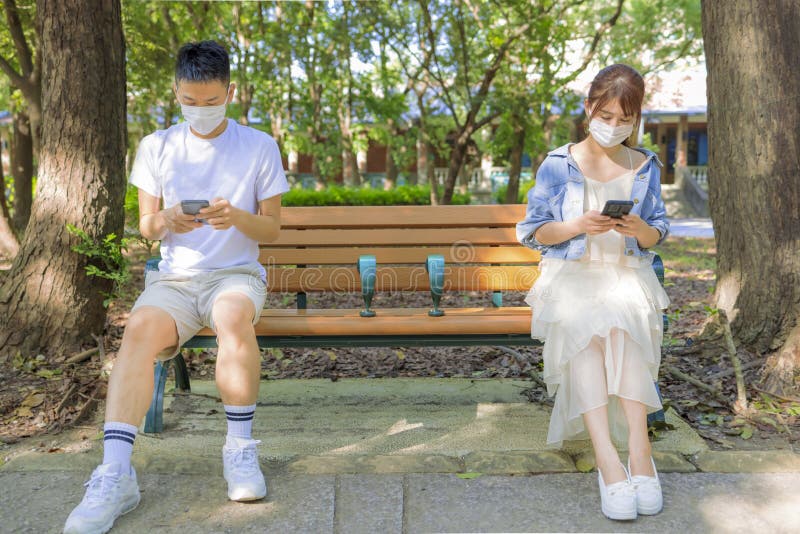 Young couple in social distancing and  sitting on the bench in park