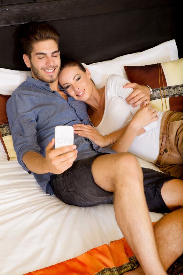 Young couple using a smartphone in a asian hotel room while lying on the be...