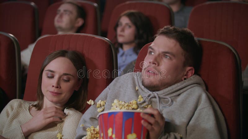 Young couple watching horror film in movie theatre. Guy sprinkle popcorn