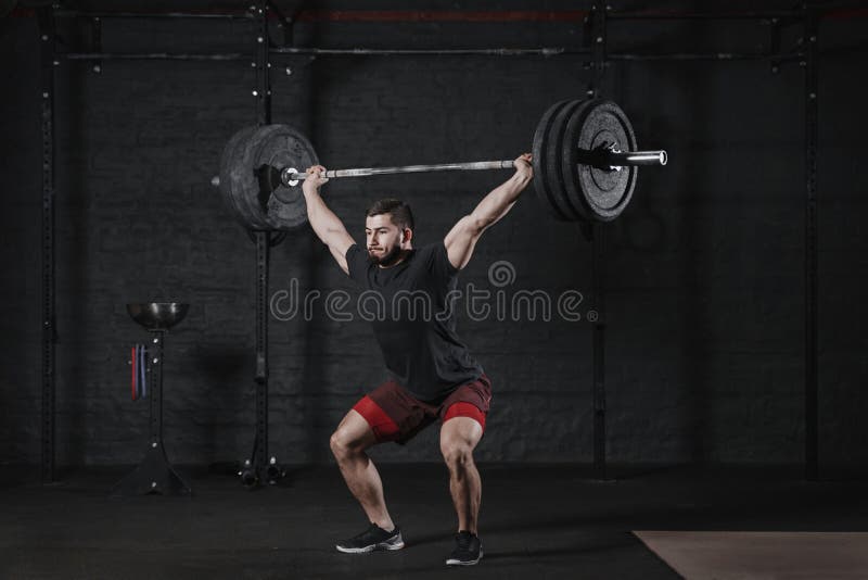 Young crossfit athlete lifting barbell overhead at the gym. Man practicing functional training powerlifting workout exercises