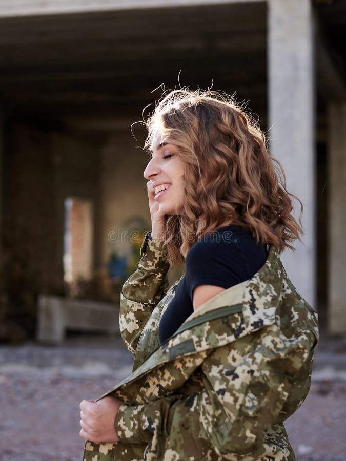 Young curly blond military woman, wearing ukrainian army military uniform and black t-shirt, posing. Three-quarter portrait of