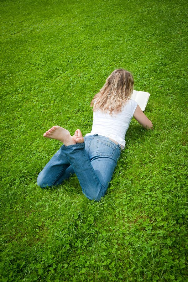 Young curly blond woman reading a book in a park