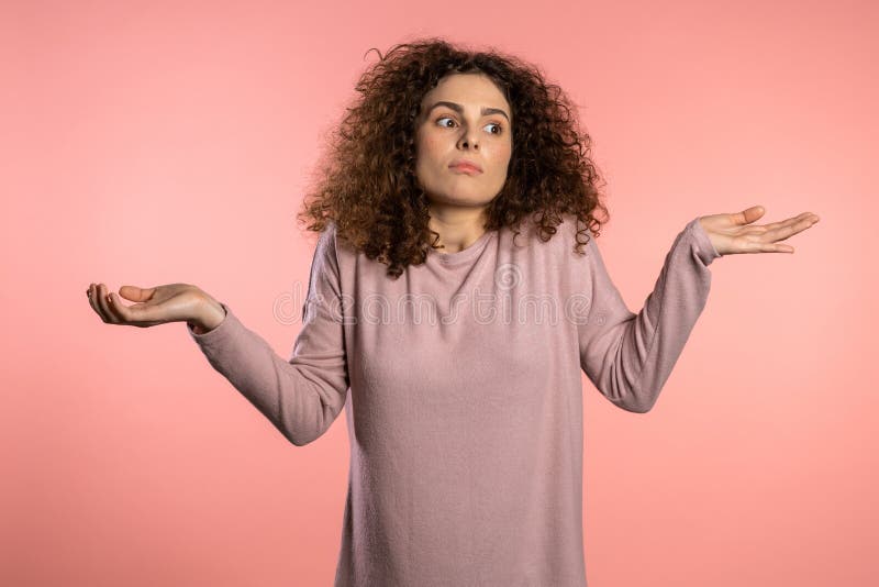 Young curly unsure girl shrugs her arms, makes gesture of I don`t know, care