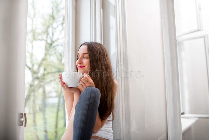 Young and cute lady dreaming on the windowsill with cup of coffee