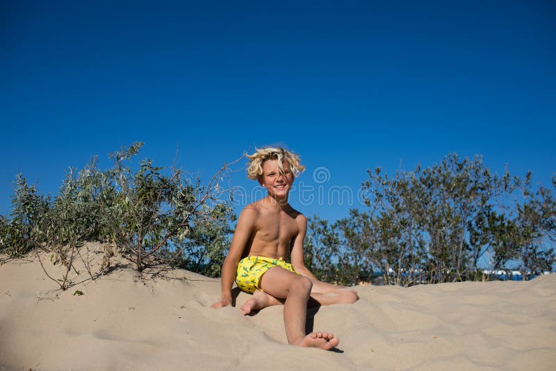 Young teen boy in yellow swim shorts posing on a sand hill at the beach.  Copy space. Stock Photo